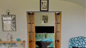 Um quarto com uma cama, um sofá, uma poltrona, uma mesinha de consola e um porta-retrato na parede.