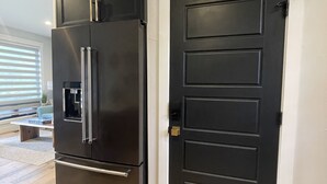 Eine moderne Küche mit einem schwarzen Kühlschrank, einer schwarzen Tür und Holzboden.