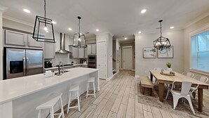 Cozinha moderna com armários brancos, uma ilha grande e iluminação pendente.