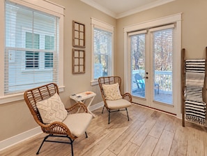 A room with two wicker chairs, a small table, and a view through a glass door to an outdoor area.