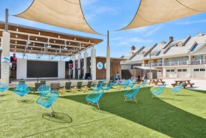 An outdoor seating area with chairs and tables, a stage, and a building with a wooden facade.