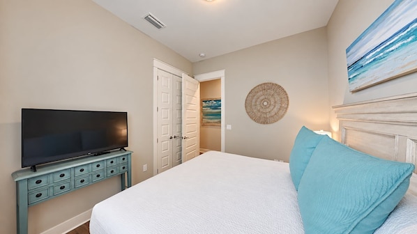 A bedroom with a bed, a television on a dresser, a door, and a wall decoration.