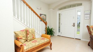 A foyer with a wicker sofa, a potted plant, a wooden staircase, and a white door. - Beautiful 5 Star Villa with Private Pool on the Prestigious Windsor Hills Resort, Orlando Villa 4766 (Orlando)