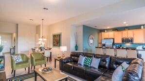 A modern living room with a leather sofa, two green armchairs, a dining area with a chandelier, and a kitchen with wooden cabinets and appliances. - 5 Star Villa on Windsor Hills Resort with Large Private Pool, Orlando Villa 4772 (Orlando)