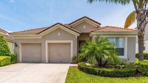 A two-story house with a tiled roof, two attached garages, and a well-maintained front yard with palm trees and shrubs. - 5 Star Villa on Windsor Hills Resort with Large Private Pool, Orlando Villa 4772 (Orlando)