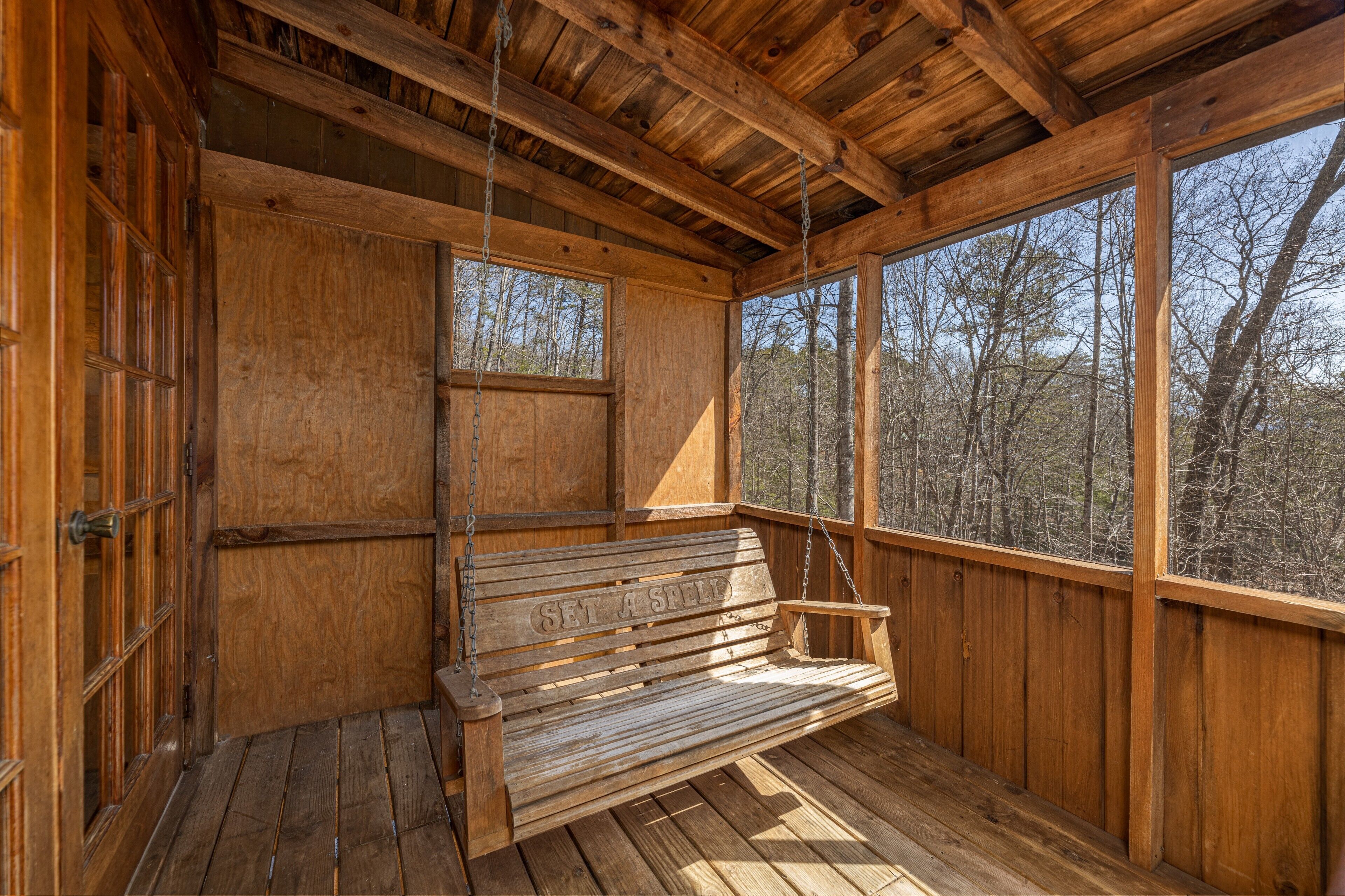 A wooden cabin with a bench and large windows overlooking a forest.
