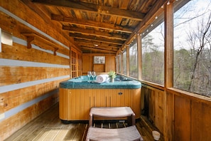 A wooden cabin with a hot tub, a bench, and a window overlooking a forest. - Secluded, Yet Convenient to All Attractions! (Sevierville)