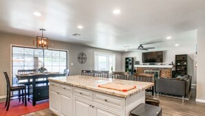 Une cuisine moderne avec des meubles blancs, un grand îlot central et un coin repas agrémenté d’un tapis rouge.