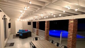 Un espace extérieur abrité comprenant une piscine, une table en bois et un coin salon avec des coussins.