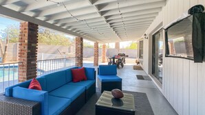 Une terrasse extérieure avec un canapé bleu, une table basse en verre et un coin barbecue à l’arrière-plan.