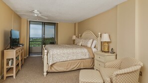 Habitación de hotel con cama, televisor, escritorio, silla y balcón con vistas.