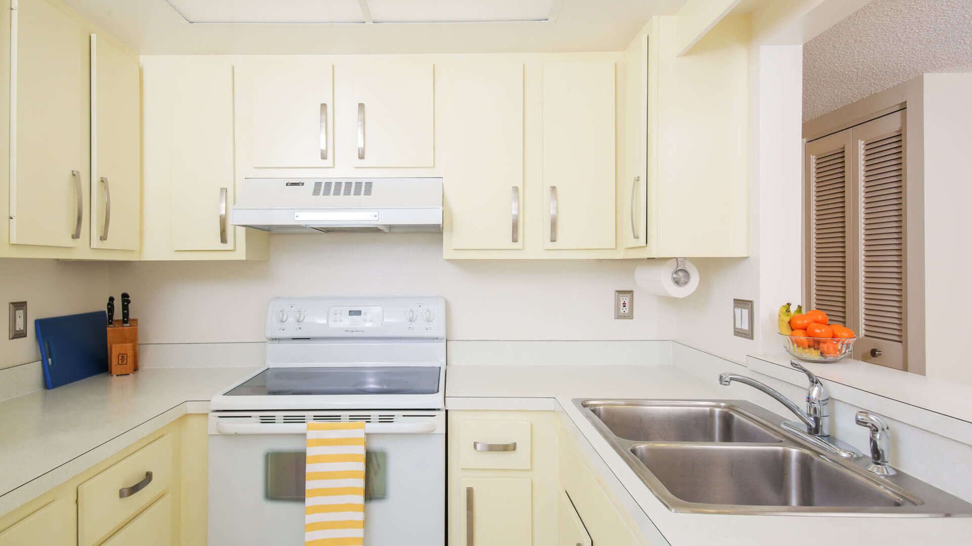 A kitchen with white cabinets, a stove, a sink, and a window with blinds.