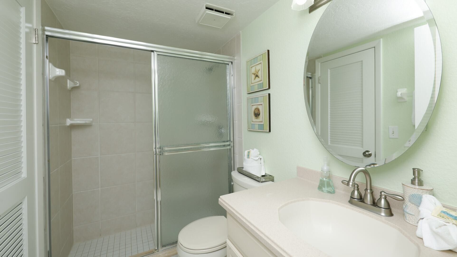 Une salle de bain avec une douche à parois de verre, des toilettes, un lavabo avec un miroir et deux tableaux encadrés au mur.