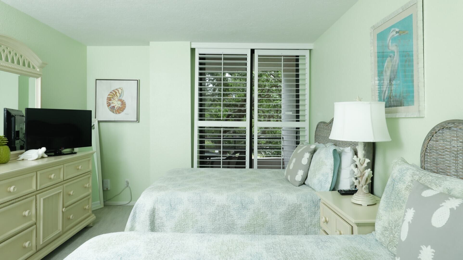 Une chambre à coucher comprenant un lit, une commode, un téléviseur et une fenêtre avec des stores.
