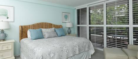 A bedroom with a large bed, a nightstand, a chair, and a window with blinds.