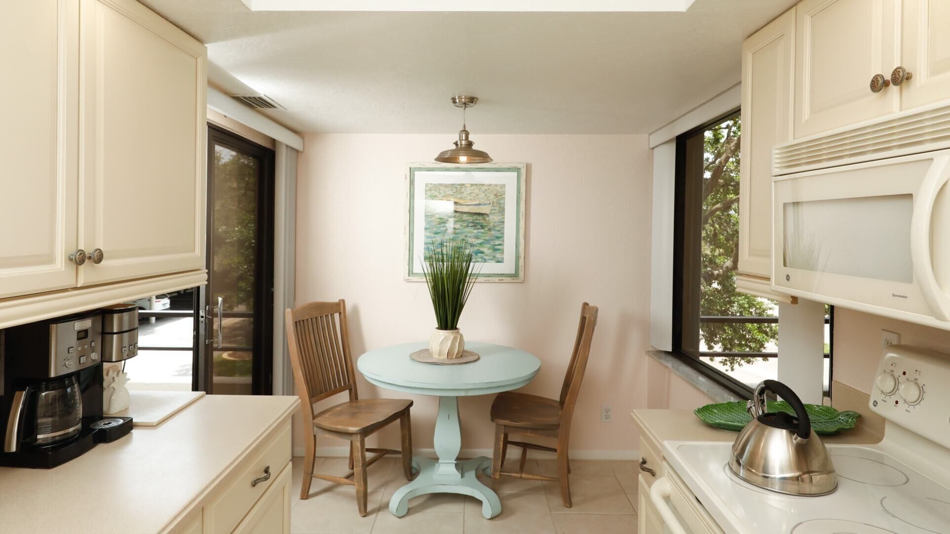 A compact kitchen with a dining table, chairs, a coffee maker, a kettle, and a microwave.