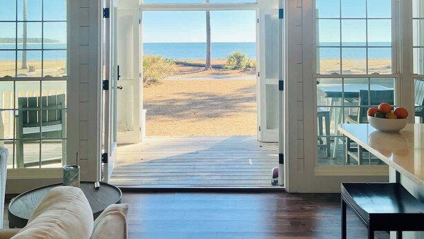 A room with a view of the beach, a sign that says "SEAS THE DAY", and a dining area with a table and chairs.