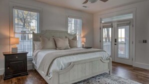 A bedroom with a bed, nightstands, a ceiling fan, and large windows.