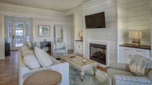 A spacious living room with a fireplace, a sofa set, a coffee table, and a television mounted on the wall.