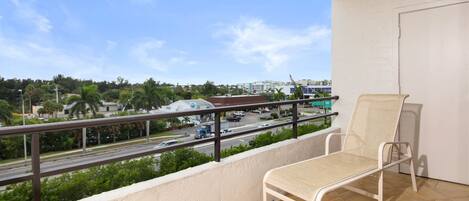 A balcony with a white chair, a view of a road with vehicles, and buildings in the background.