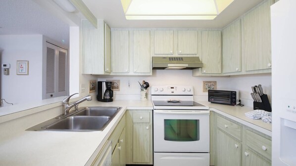 A kitchen with white cabinets, a stainless steel sink, a coffee maker, a stove, and a toaster.