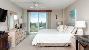 A hotel room with a large bed, a dresser, a desk, a ceiling fan, a large window with a view, and a painting on the wall. - Perfect 2 Bedroom Apartment on The Anchorage, Siesta Key Apartment 1020 (Siesta Key)