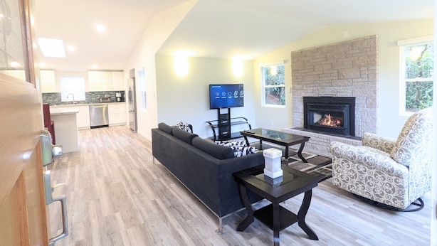 A modern living room with a fireplace, a television, and a dining area with a table and chairs. - Cute Edmonds Bowl Cottage (Edmonds)