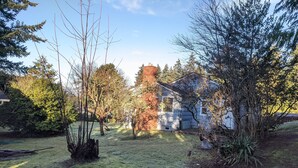 A residential area with a grassy yard, trees, and a house with a red chimney. - Cute Edmonds Bowl Cottage (Edmonds)