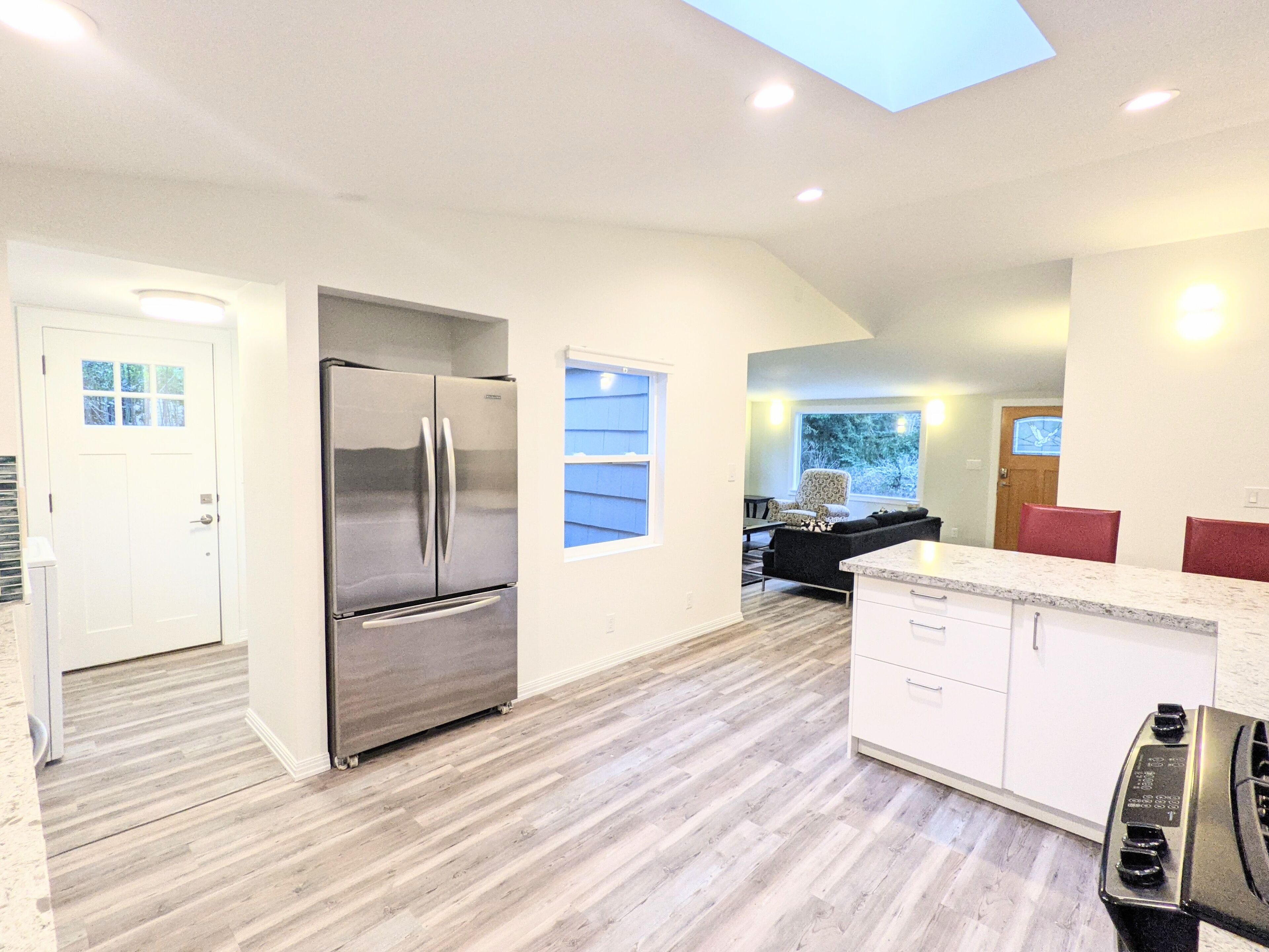 A modern kitchen with a stainless steel refrigerator, white cabinetry, and a skylight.