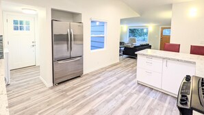 A modern kitchen with a stainless steel refrigerator, white cabinetry, and a skylight. - Cute Edmonds Bowl Cottage (Edmonds)