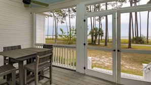 A covered porch with a table and chairs, overlooking a beach with trees and a grassy area. - Angel Oak Cottage-5bdrm Luxury and Beachfront-4 Pass Golf Cart Included (Daufuskie Island)