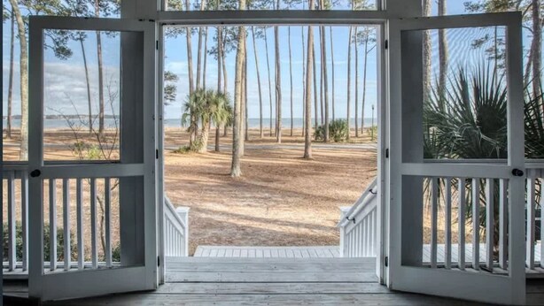 An open wooden door leading to a sandy beach with tall trees and a clear sky. - Angel Oak Cottage-5bdrm Luxury and Beachfront-4 Pass Golf Cart Included (Daufuskie Island)