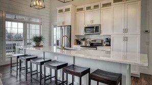 A modern kitchen with white cabinets, a large island with bar stools, stainless steel appliances, and pendant lighting. - Angel Oak Cottage-5bdrm Luxury and Beachfront-4 Pass Golf Cart Included (Daufuskie Island)