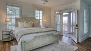 A bedroom with a bed, two bedside lamps, a ceiling fan, and a view through the open door. - Angel Oak Cottage-5bdrm Luxury and Beachfront-4 Pass Golf Cart Included (Daufuskie Island)