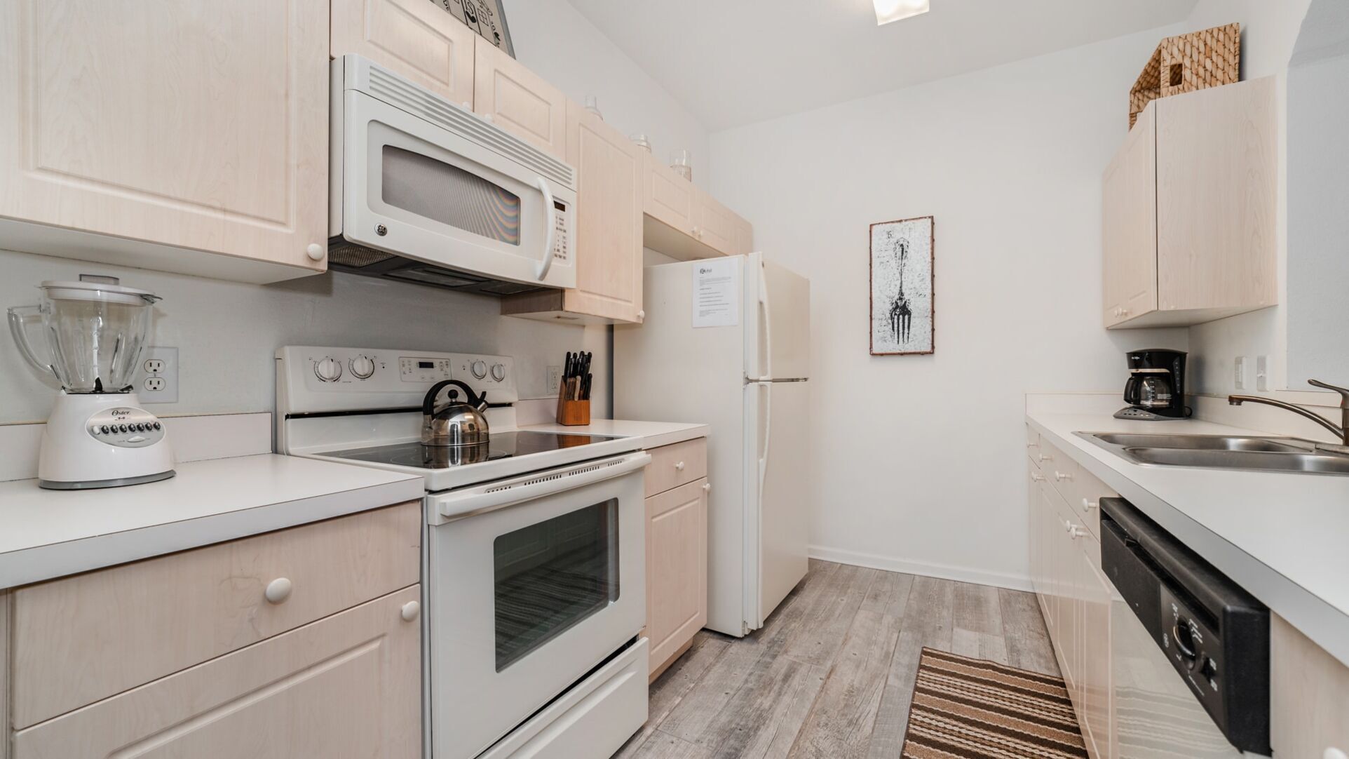 A modern kitchen with white appliances, wooden cabinets, and a stainless steel sink.