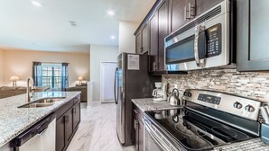 A modern kitchen with granite countertops, stainless steel appliances, and a backsplash of small tiles. - Beautiful 5 Star Townhome on Storey Lake Resort with Private Pool, Orlando Townhome 4807 (Orlando)