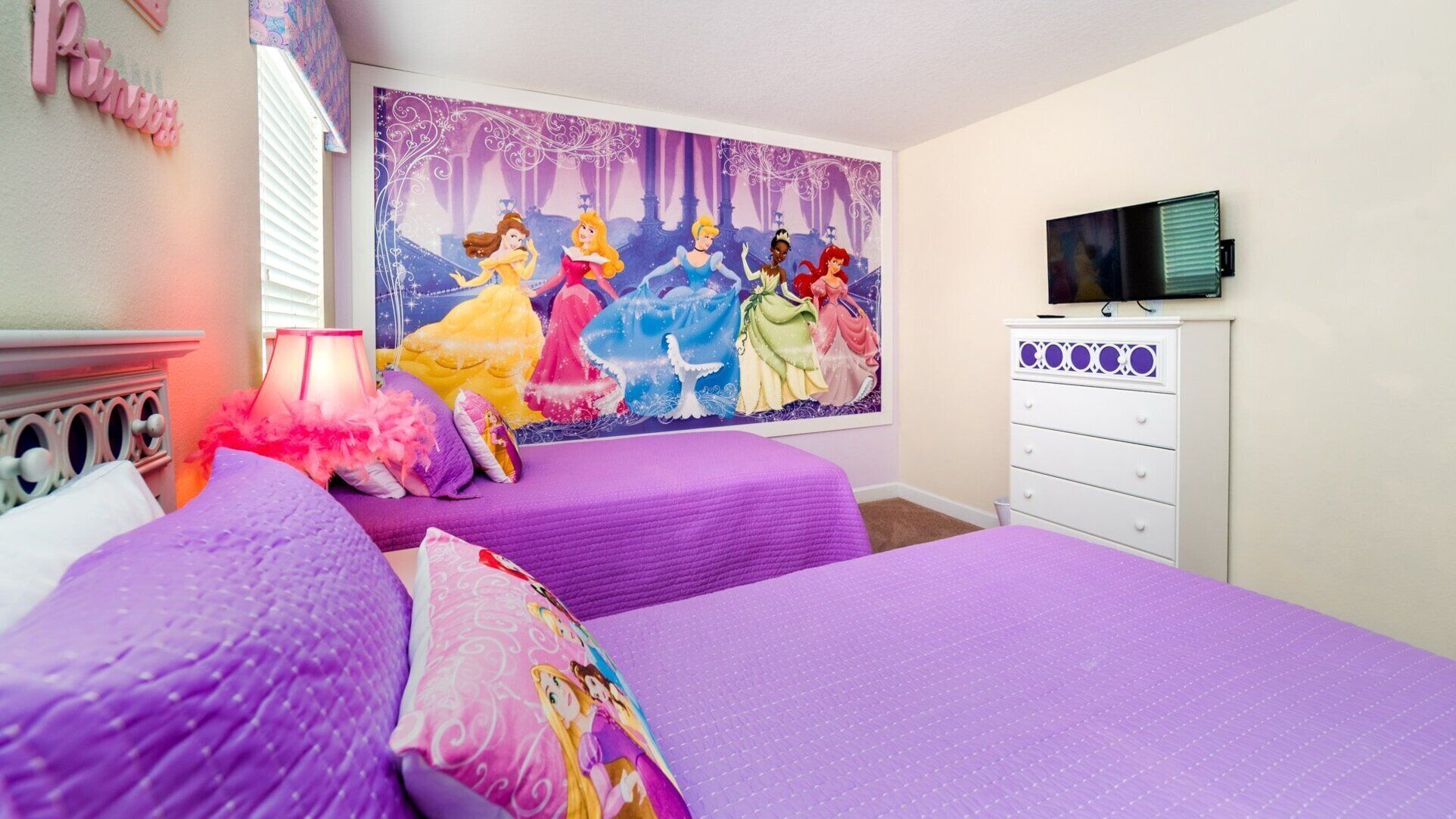 Un dormitorio con dos camas, un televisor y un gran mural de princesas Disney en la pared.