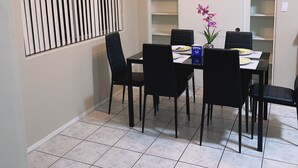 Ein Essbereich mit Tisch für vier Personen, schwarzen Stühlen, einem Deckenventilator und einem Fenster mit Jalousien.