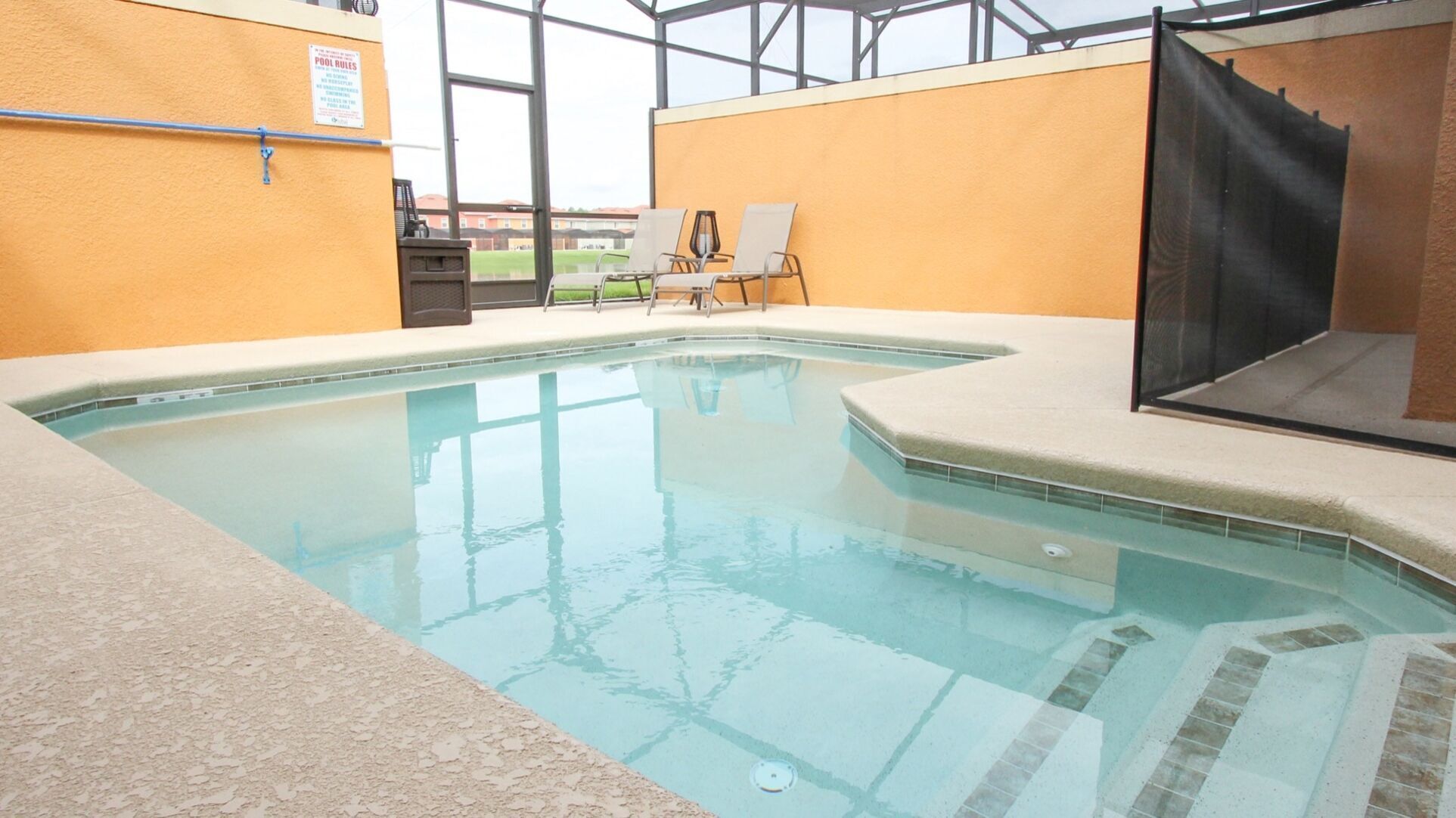 Ein Innenpool mit klarem Wasser, umgeben von beige gefärbten Wänden und einer Glasdecke. Auf einer Seite befinden sich Liegestühle und ein schwarzer Bildschirm.