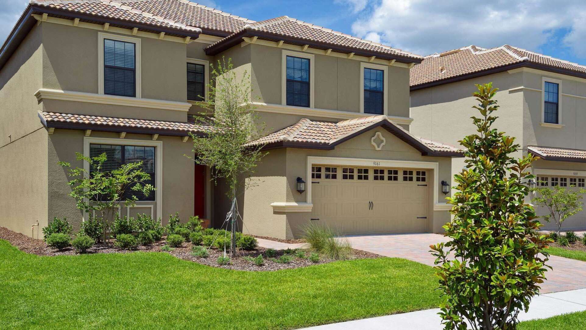 A two-story residential building with a beige exterior, a tiled roof, and a front garage.