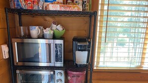 Cucina con forno a microonde, tostapane e macchina del caffè su un ripiano, un piccolo frigorifero e un cestino.