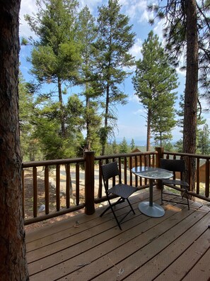 A wooden deck with a table and chairs, surrounded by tall pine trees and a clear sky. - Gated Luxury Queen Bed Cottage Sleeps 2 Air Conditioning Kitchenette EV Charger (Somers)