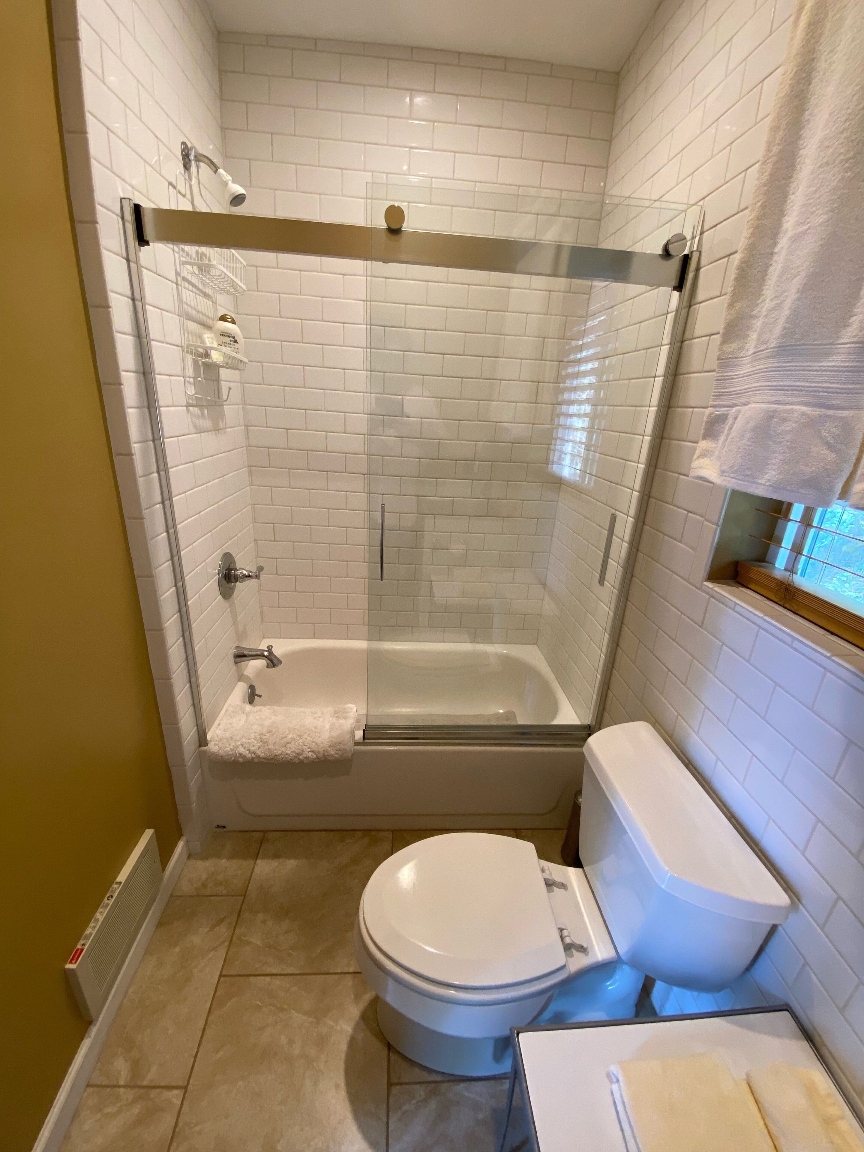 Un baño con ducha envuelta en vidrio, bañera, inodoro y perchero para toallas.