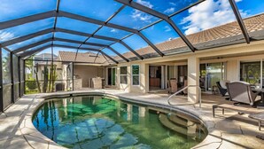 Una piscina con cerramiento de cristal, mobiliario de patio y vistas al vecindario.