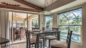 Un comedor amplio con una gran mesa y sillas, ventanas grandes con vistas a zonas verdes y un techo con vigas de madera a la vista.