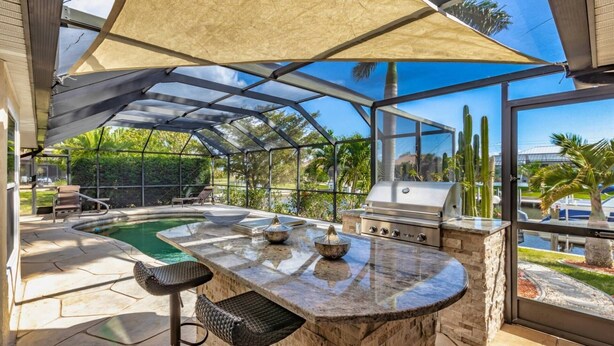 Una cocina al aire libre techada con una parrilla, una piscina y un área de estar.
