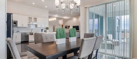 A modern kitchen with white cabinets, a central island, and a dining area with a dark wooden table and grey upholstered chairs.