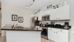 A modern kitchen with white cabinets, a granite countertop, stainless steel appliances, and decorative wall art.