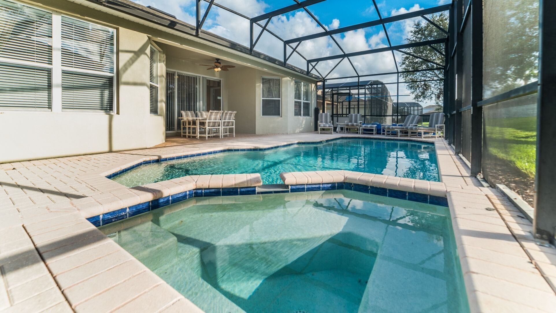 A swimming pool with a tiled edge, surrounded by a covered patio area with chairs and a table.
