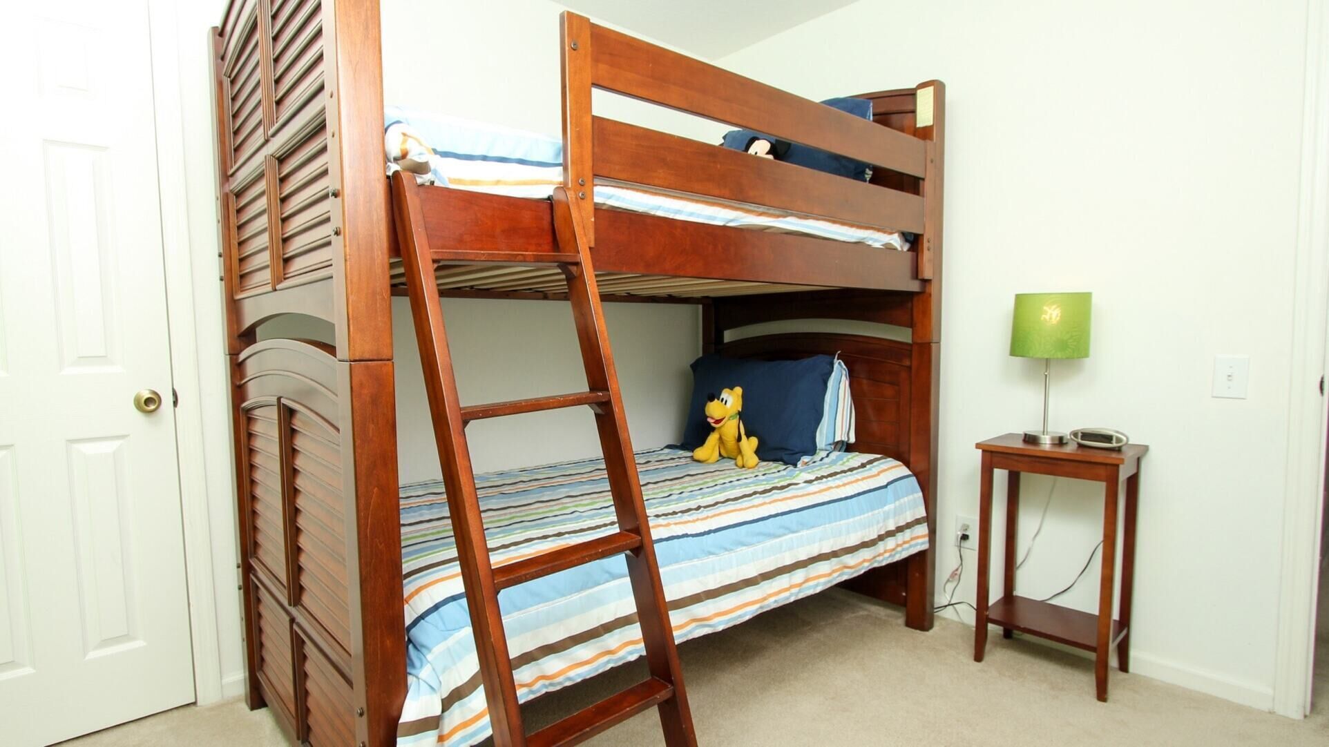 A bunk bed with a ladder, a small bedside table, a lamp, and a plush toy on the lower bunk.